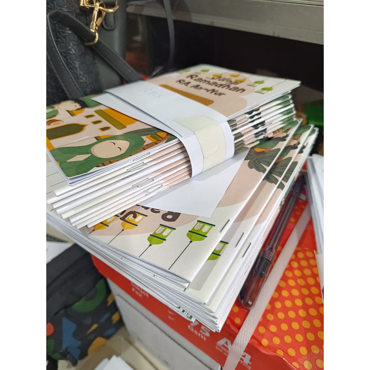 Tumpukan hasil cetak booklet A5 jurnal Ramadhan dengan sampul warna di OSC Makassar